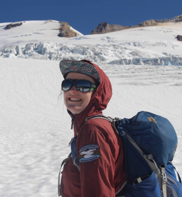 Mariama (woman with pale skin and brown hair, wearing a hat and bundled up in a jacket) stands on a glacier in the North Cascades